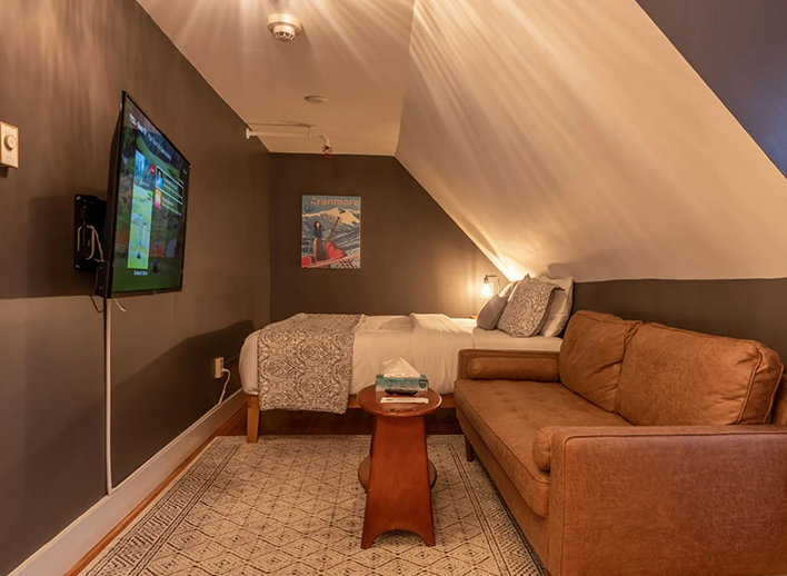 Hotel suite with a T V mounted on the wall and a leather loveseat and a queen bed in North Conway